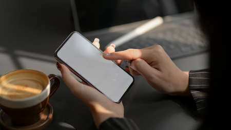 Cropped shot of businesswomen typing on blank screen smartphone with office supplies and coffee cup...