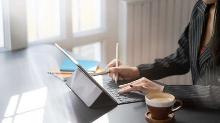 Cropped shot of businesswomen working on digital tablet with office supplies and coffee cup while...