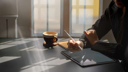 Side view of female freelancer working on digital tablet while sitting next to window in coffee shop