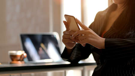 Cropped shot of female using smartphone with tablet and coffee cup on black table in comfortable...