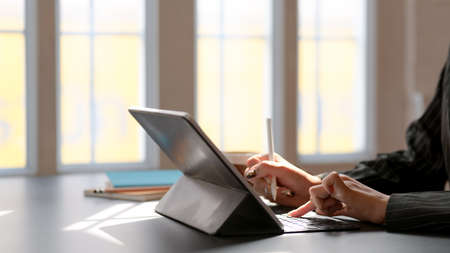 Cropped shot of female working on digital tablet with stylus and other office supplies on black desk...