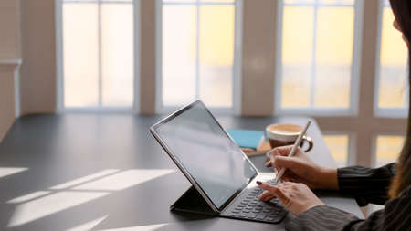 Side view of female working on digital tablet with stylus and other office supplies on black desk in...