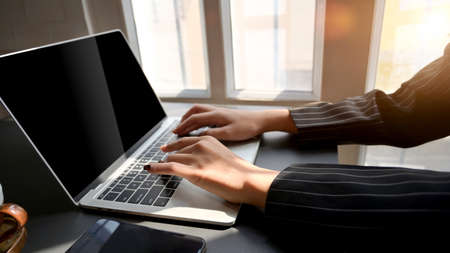 Side view of female typing on laptop with smartphone on black table in comfortable workplaceの写真素材