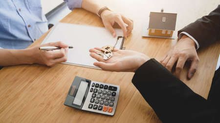 Side view of real estate agent holding house key to his customer while signing contract agreementの写真素材