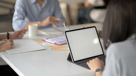 Cropped shot of female app developer typing on mock up tablet while discussing with her UI developer...