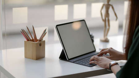 Cropped shot of female designer typing on blank screen tablet with wooden figure and coloured...