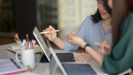Side view of young professional designer team consulting on their project with digital tablet in...