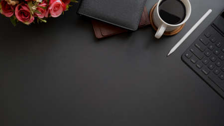 Top view of dark modern workplace with copy space, wireless device, roses vases and coffee cup on black table backgroundの写真素材