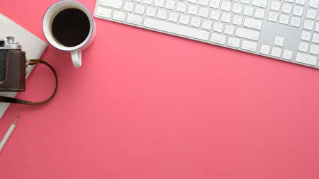 Overhead shot of stylish photographer workspace with computer, coffee cup, camera and copy space on pink table backgroundの写真素材