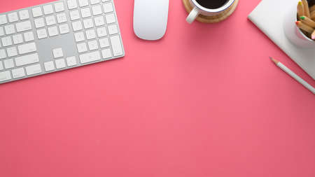 Overhead shot of stylish designer workspace with computer, stationery, coffee cup and copy space on pink table backgroundの写真素材