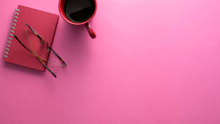 Top view of stylish workspace with notebook, glasses, coffee cup and copy space on pink table backgroundの写真素材