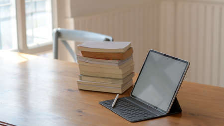 Cropped shot of blank screen tablet and books on wooden table in comfortable working space の写真素材