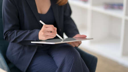 Cropped shot of businesswoman writing on blank screen tablet with stylus while sitting in simple workplace の写真素材