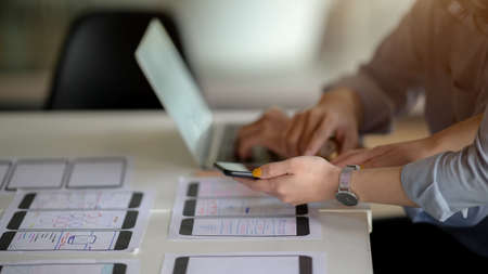 Side view of UI developer working on  laptop and document on white desk while consulting with co...
