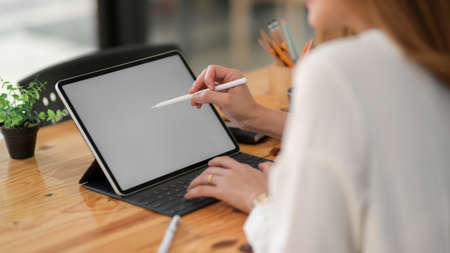 Cropped shot of female freelancer drawing on blank screen tablet with stylus while sitting in simple...