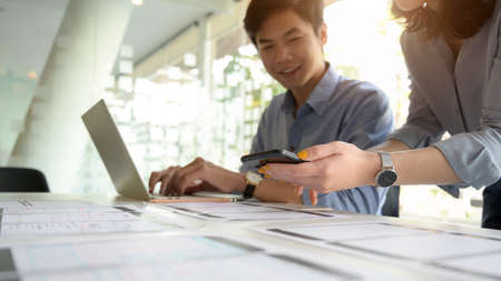 Cropped shot of UI developer working on  laptop and document on white desk while consulting with co...