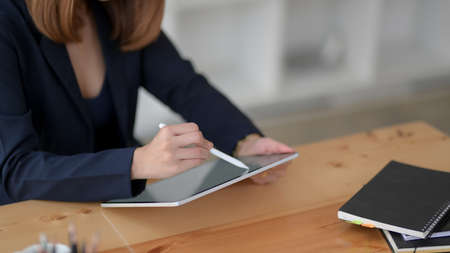 Cropped shot of businesswoman writing on blank screen tablet with stylus and office supplies on wooden desk の写真素材