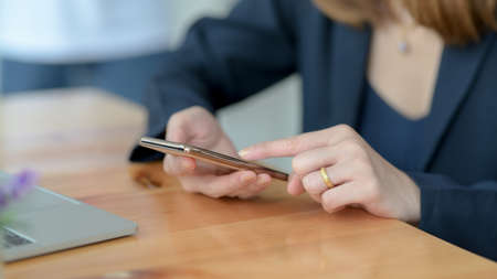 Close up view of a woman touching on smartphone with laptop on wooden desk background