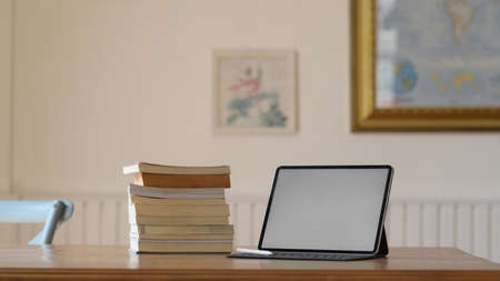Close up view of simple workplace with mock up digital tablet and books on wooden desk in living...