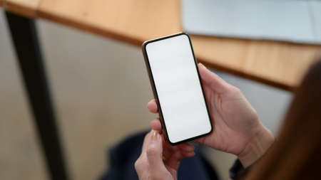 Close up view of a woman using blank screen smartphone while sitting in simple workplaceの写真素材