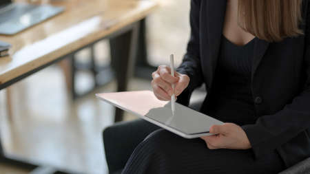 Cropped shot of female freelancer drawing on blank screen tablet with stylus while sitting in simple workplace の写真素材