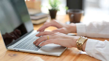 Side view of a woman typing on laptop on wooden desk with coffee cup and office supplies 