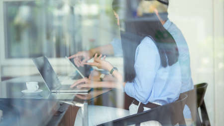 Shot through a glass window  of two businessperson consulting on their work while sitting in...
