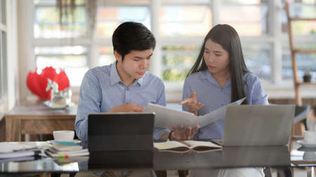 Cropped shot of two businesspeople consulting on their work with tablets and office supplies while sitting in simple co-working space の写真素材