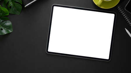 Overhead shot of dark modern workplace with mock up tablet, office supplies and coffee cup on black table backgroundの写真素材