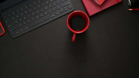 Top view of stylish workplace with wireless keyboard, office supplies, copy space and red coffee cup on black table background の写真素材