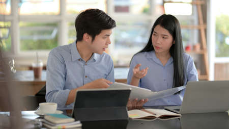 Cropped shot of two businesspeople consulting on their work with tablets and office supplies while sitting in simple co-working space の写真素材