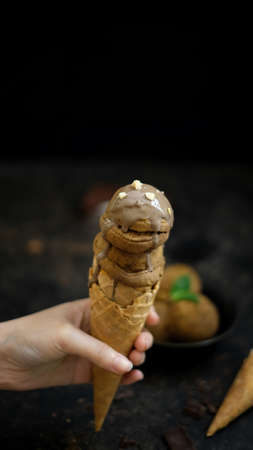 Cropped shot of a girl holding chocolate ice-cream cone on blurred dark backgroundの写真素材
