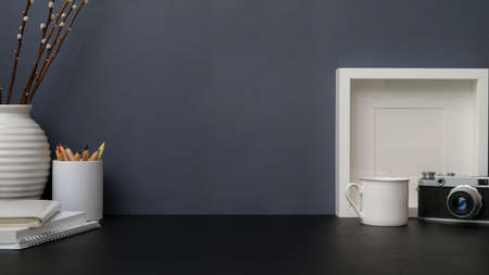 Cropped shot of trendy photographer workplace with copy space, frame camera and stationery on black table with grey wall background の写真素材