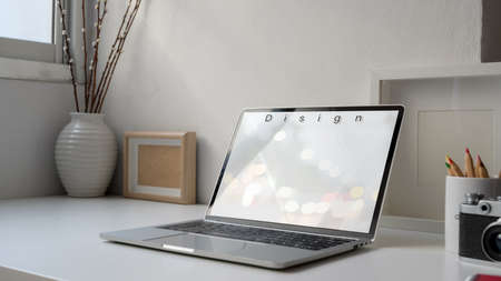 Cropped shot of modern workplace with blank screen laptop, mock up frames and decorations on white...