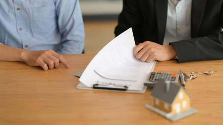 Cropped shot of real estate agent explaining contract to customer with house model and supplies on...