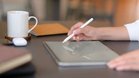 Close up view of young college girl writing on mock up tablet while working on her project with...