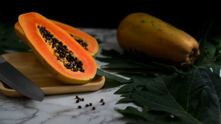 Cropped shot of whole and slice of sweet papaya on wooden plate and papaya leaves on marble table の写真素材