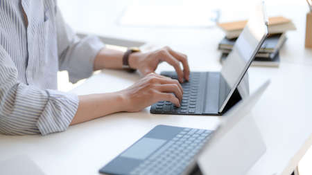 Side view of male entrepreneurs typing on laptop with tablet and other office supplies on white...