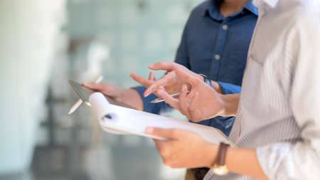 Side view of two businesspeople consulting on their work with mock up tablet and document file while...