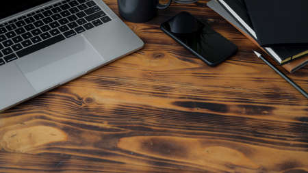 Cropped shot of modern rustic workspace with laptop, smartphone, stationery and copy space on rustic wooden desk backgroundの写真素材