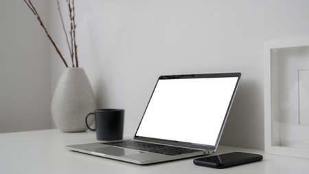 Cropped shot of simple workspace with blank screen laptop, smartphone and decorations on white desk...
