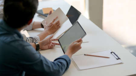 Cropped shot of two businesspeople consulting on their work with mock up tablet, document file and notebook on white deskの写真素材