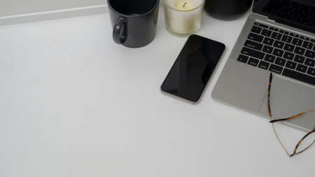 Cropped shot of minimal workspace with laptop, smartphone, decorations and copy space on white table...