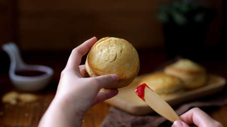 Close up view of a woman holding scone ready to put strawberry jam on scone, Traditional British...