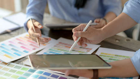 Cropped shot of two young designers consulting for choosing colour for their project on colour swatch and tablet on wooden deskの写真素材