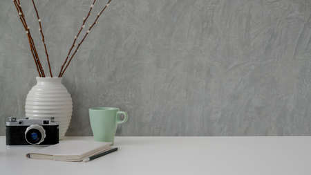 Close up view of minimal workplace with camera, stationery, mug, decoration and copy space on white...