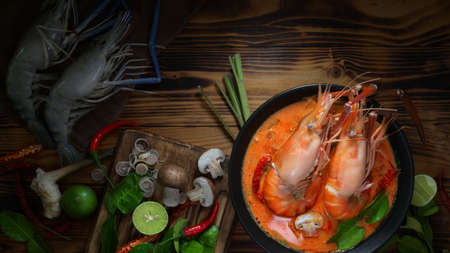 Top view of Tom yum goong, Thai traditional food with prawns, hot spicy soup in black bowl and Thai herb ingredients on wooden tableの写真素材