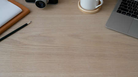 Cropped shot of trendy workspace with laptop, camera, stationery and copy space on wooed desk  