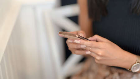 Cropped shot of young female freelancer typing on smartphone while sitting on chair in modern working spaceの写真素材