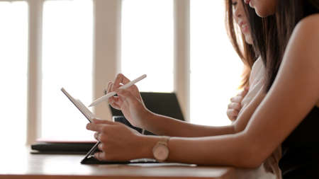 Close up view of two young college girl concentrating on their assignment with laptop and tablet  in modern living roomの写真素材
